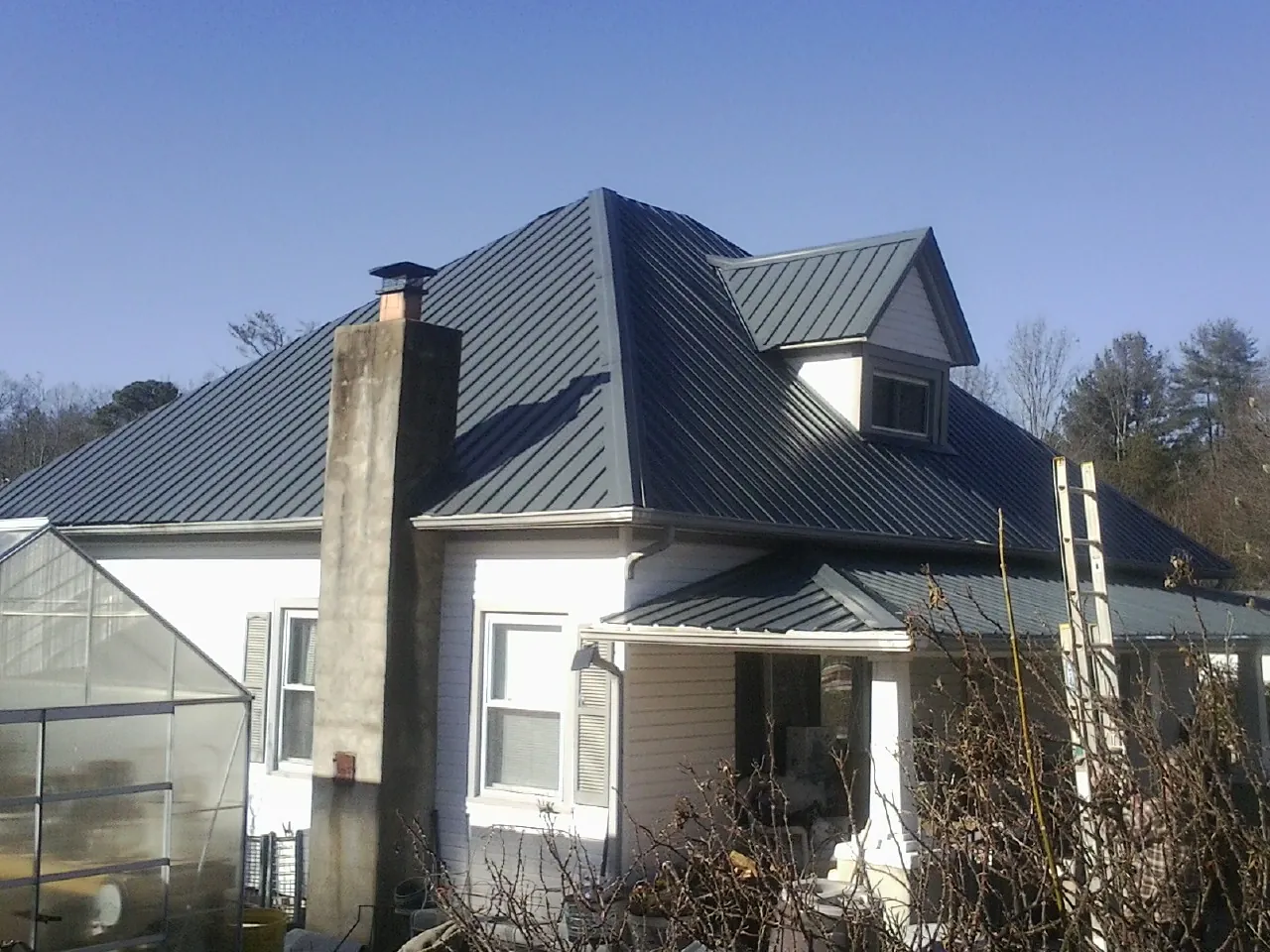 Dark blue standing seam metal roof on a white farmhouse with dormer — Slate & Tile Roof Repair by Roofing Brothers in Bidwell