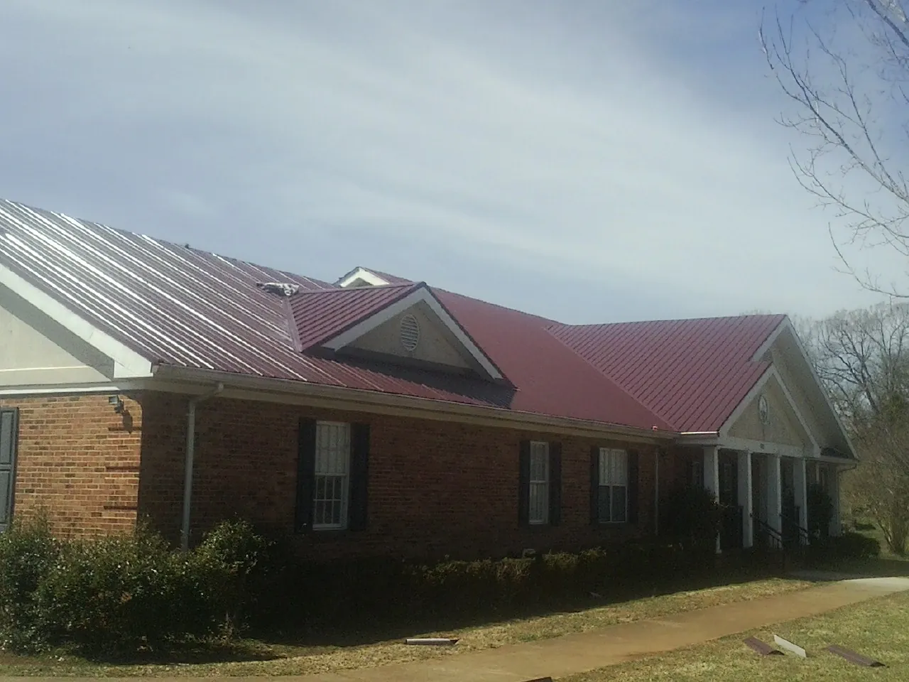 Red metal roof with gabled entries on a long brick building, from a Hail Damage Roof Repair job in Bidwell