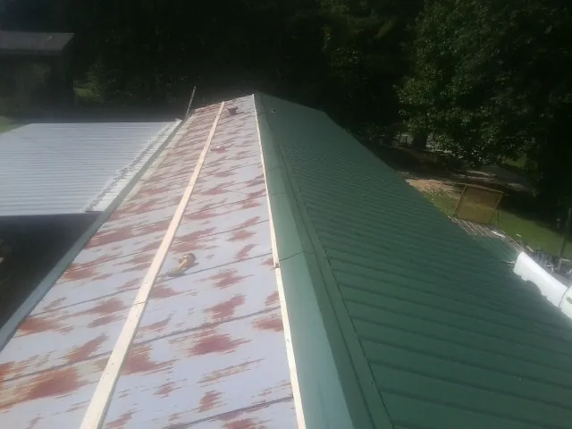 Old rusted panels beside newly installed green metal roofing — Wind Damage Roof Repair by Roofing Brothers in Bidwell