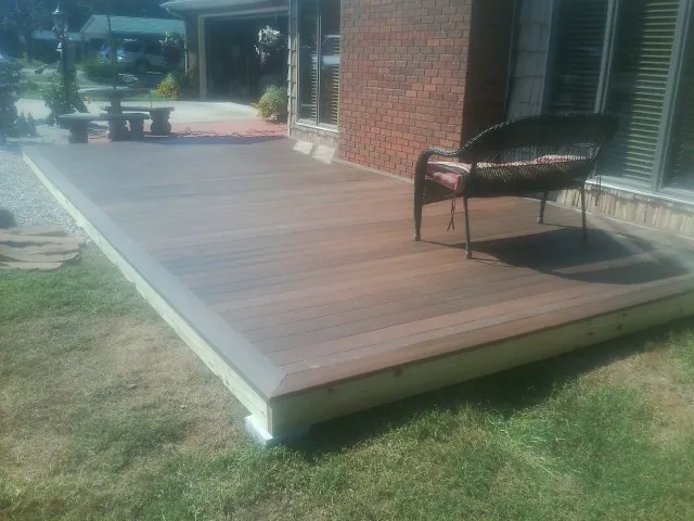 New wood deck and wicker chair beside a brick house in Bidwell
