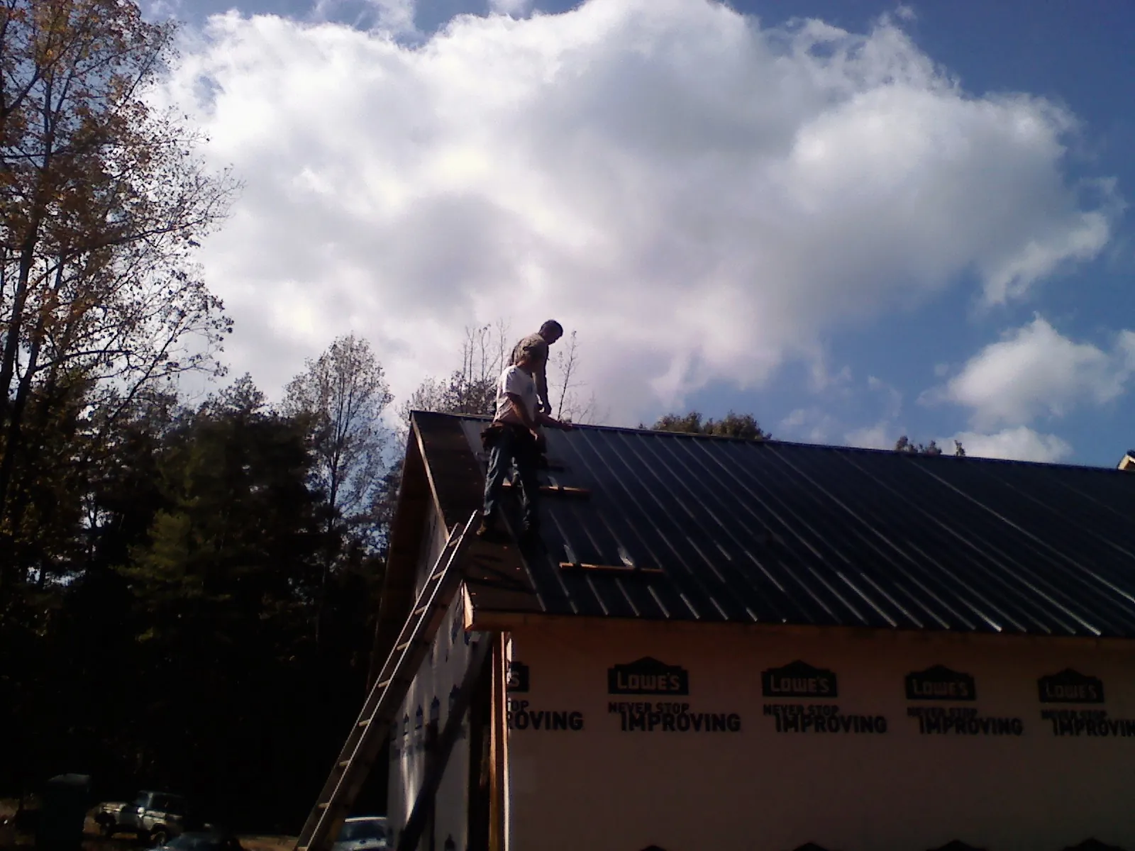 Roofer fastening dark metal panels high against a cloudy sky, from a Roof Inspection job in Bidwell