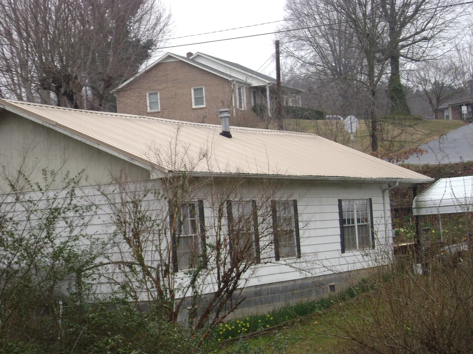 Tan metal roof on a white sided house set into a hillside — Commercial Roofing by Roofing Brothers in Bidwell